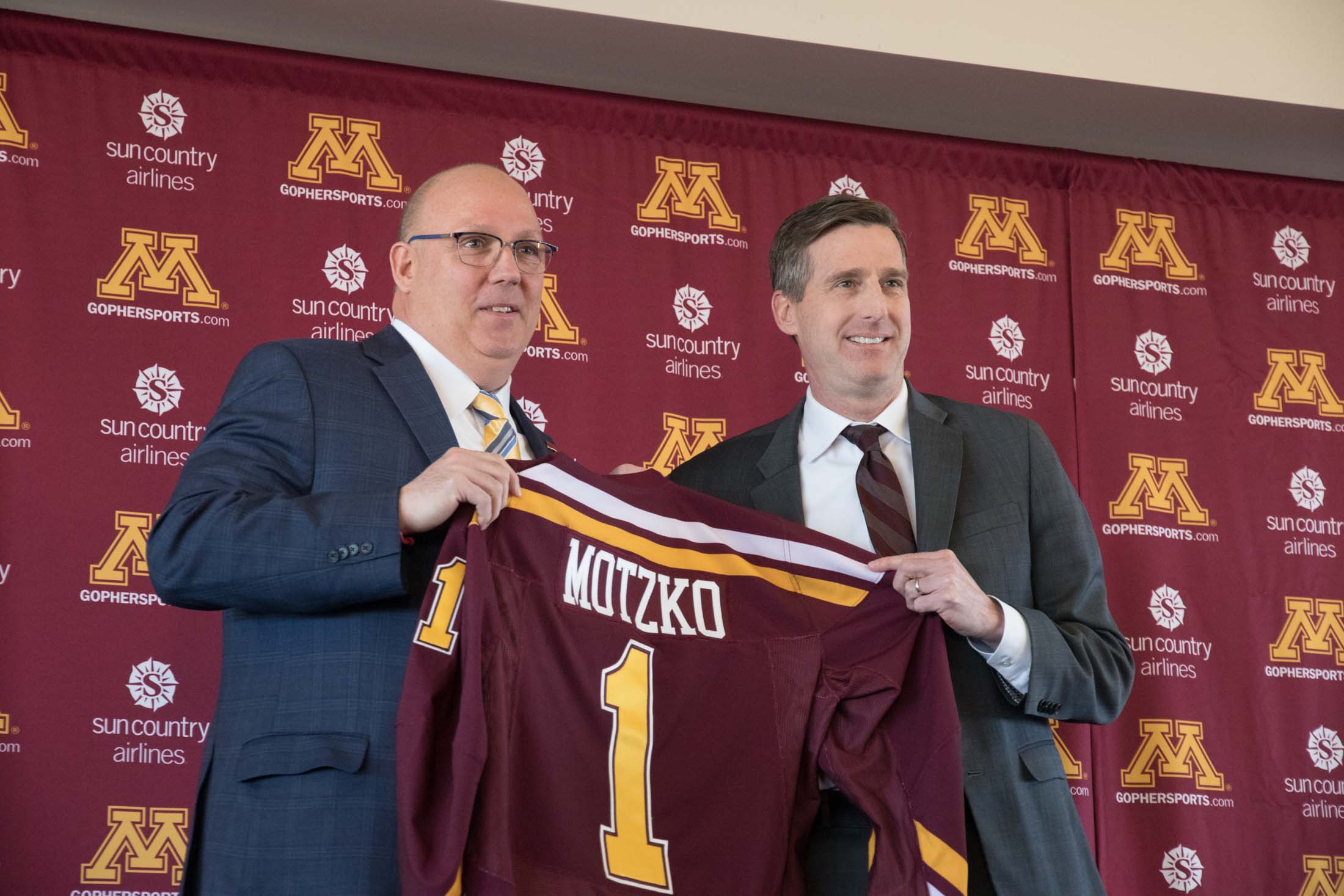 Bob Motzko and Mark Coyle holding a maroon Minnesota hockey jersey with Motzko's name on the back